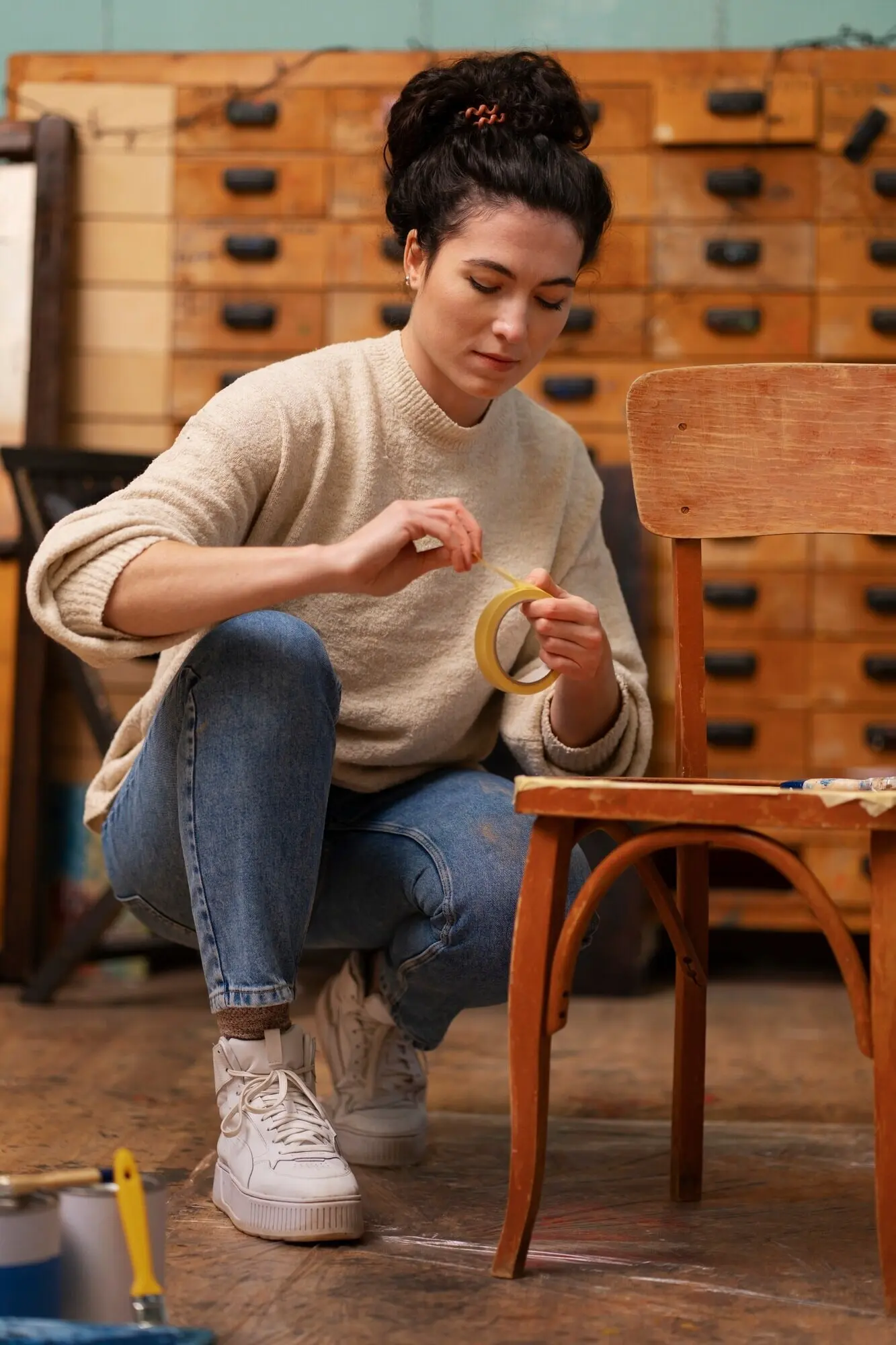 Ganzkörperaufnahme einer Frau, die einen Holzstuhl restauriert.